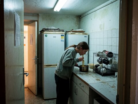 Young woman eating noodles from a pot in a run-down communal kitchen