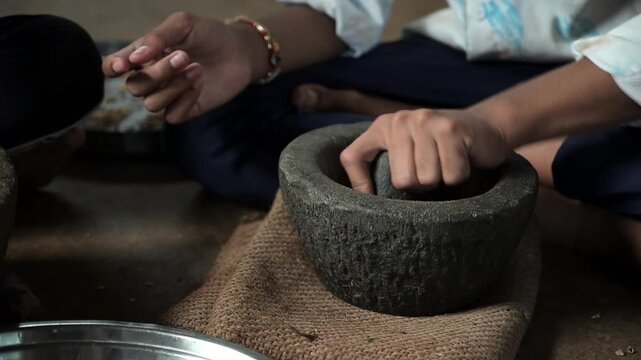 Close-up video footage of a person's hands using a traditional stone mortar and pestle (okhli) to grind spices by hand, a time-honored method still practiced in rural Indian households.