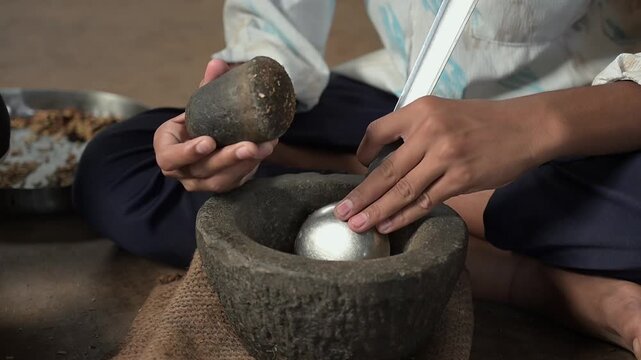 Close-up video footage of a person's hands using a traditional stone mortar and pestle (okhli) to grind spices by hand, a time-honored method still practiced in rural Indian households.