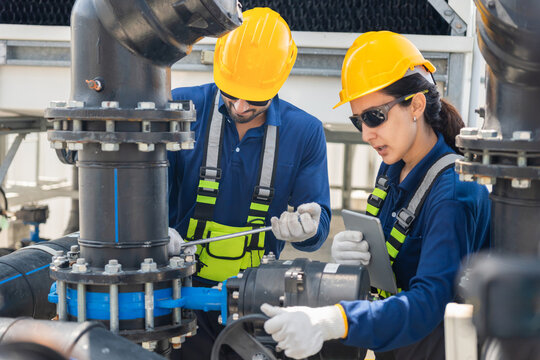 Industrial engineers inspecting pipes and valves equipment in factory cooling system, maintenance team checking water pipe infrastructure and machinery in industrial facility