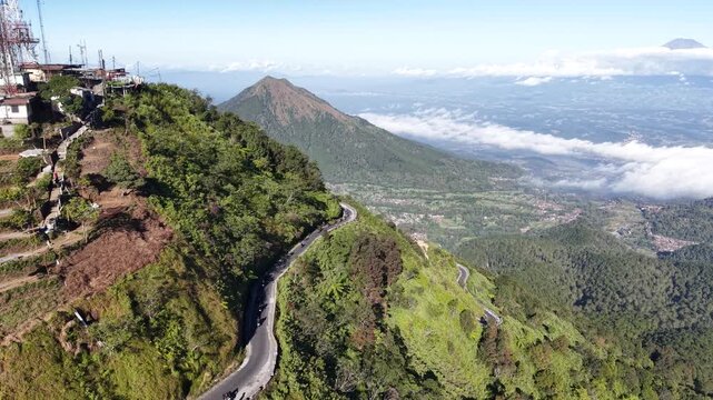 Drone aerial footage of motorcycle riders navigating scenic winding mountain roads on Mount Telomoyo in Central Java, Indonesia, showcasing adventure travel.