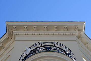 A low angle view of a historic building roof line decorated with ornate cornices and a rounded black metal balcony. © nahhan