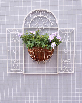 White wrought iron arched window frame with hanging basket of purple verbena flowers on gray tile wall