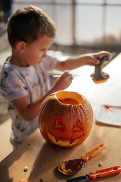 Cute kid carving and painting a spooky halloween pumpkin. Arts and crafts theme. 
