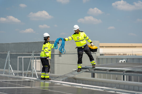 Solar panel technicians working together on rooftop passing cable for renewable energy project, engineers maintenance team handling equipment and rope installing photovoltaic system on building roof