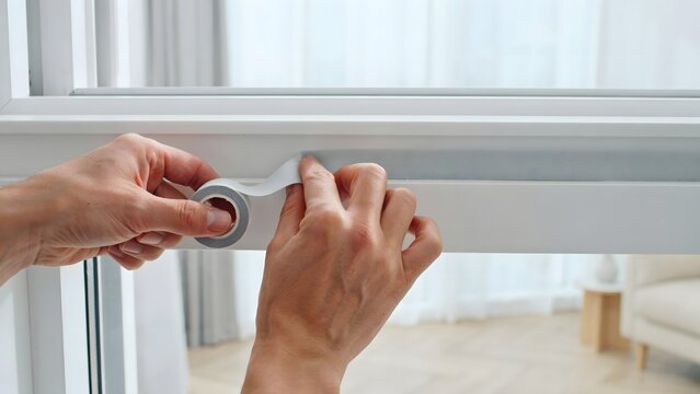 Hands Unrolling White Weatherstripping onto a Window Frame