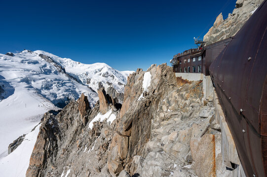 Alpinists climbing the iconic Ar&ecirc;te du Cosmique near Aiguille du Midi with Mont Blanc in the background, surrounded by dramatic rocks and snow under a clear blue sky. Powerful alpine adventure scene.