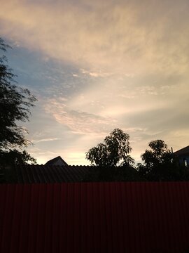 Beautiful sunset sky with clouds over a red fence and tree silhouettes