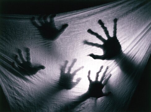 Spooky silhouette of monster hands scratching and gesturing behind translucent sheet