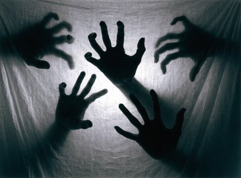 Ghostly zombie hands scratching behind a white translucent plastic backdrop screen
