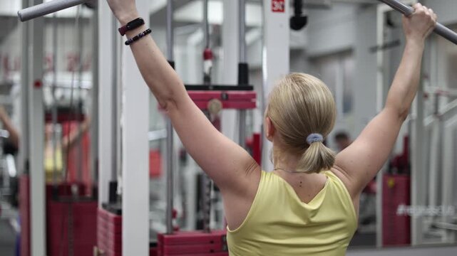 In this close-up vertical video, watch a middle-aged woman engage in pulldown training on a lat machine, showcasing her commitment to fitness and the importance of strength training in the gym.
