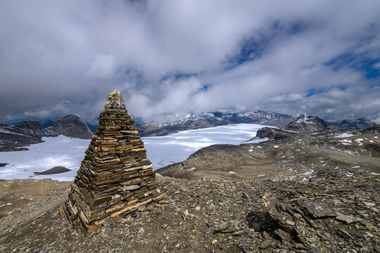 A stone pyramid cairn stands on a rocky peak overlooking the vast Plaine Morte Glacier in Valais, Switzerland
