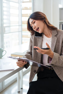 Business woman talking on phone and reading documents at table in office.
