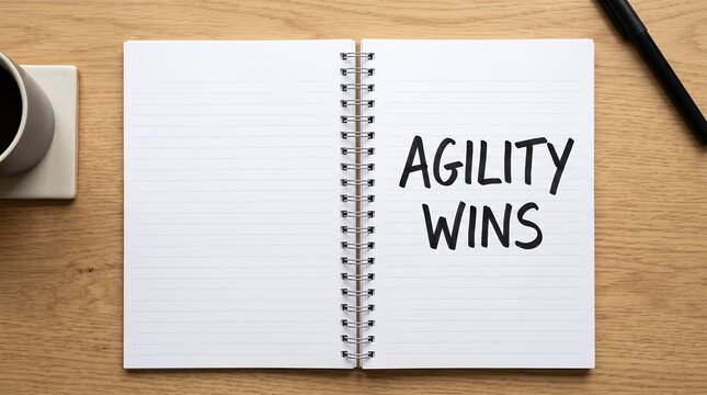 Agility Wins motivational message handwritten in bold black letters on the lined page of an open spiral notebook on a wooden desk