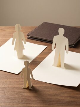 Paper cutout man woman and child standing on sheets over wooden desk