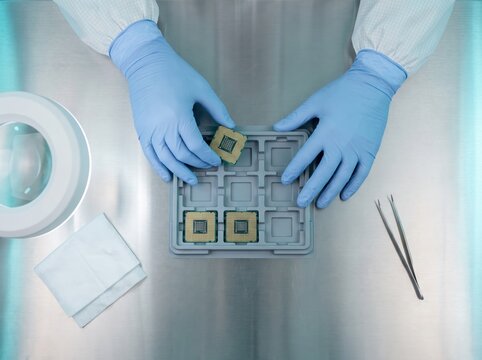 Technician in blue gloves placing processor chips into tray on steel workbench