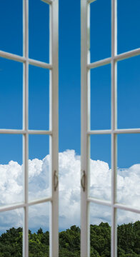 Sunny day view of blue sky through an open white wooden window