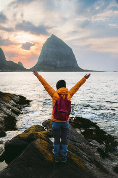 Woman tourist travel solo in Norway female holidaymaker enjoying Helgeland islands sunset view, active summer vacations adventure lifestyle tour girl with backpack happy raised hands outdoors