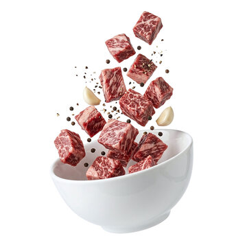 Fresh raw beef cubes with garlic and black peppercorns falling into a white bowl