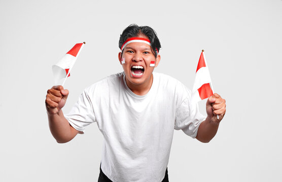 Excited young Asian man is raising his hands celebrating victory while holding country flags.
