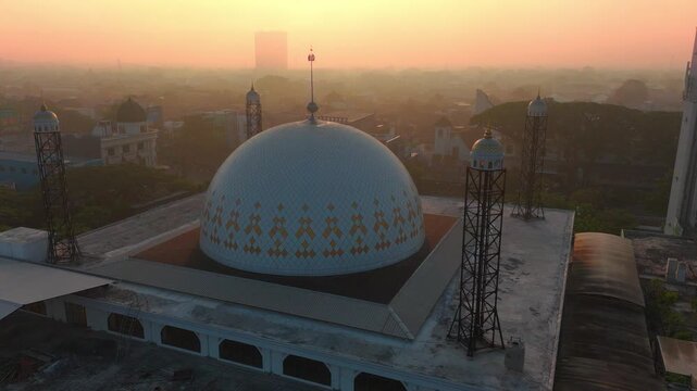 Aerial view of a mosque with a white dome and minarets during golden hour in Malang, East Java, Indonesia.