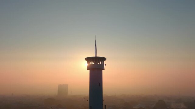 Aerial view of a mosque minaret at sunrise with a hazy urban skyline in Malang, East Java, Indonesia.