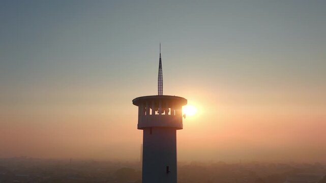 Aerial view of a tower silhouette against the warm glow of the sunrise in Malang, East Java, Indonesia.
