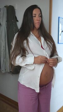 Pregnant woman trying to button up her shirt