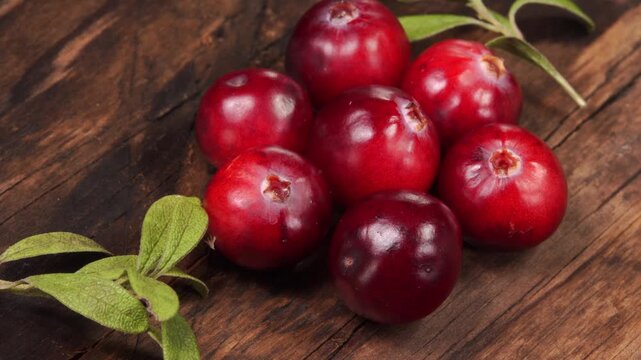 Fresh cranberries with green leaves rotating on a wooden background.