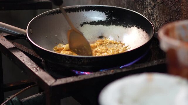 Chef using spatula to stir fry fresh squid rings with chili, garlic, and basil in a hot skillet over stove flame, showing cooking process for spicy Thai stir-fried squid concept.