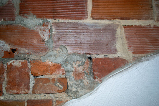 Close-up view of weathered red brick masonry with gray mortar joints showing texture and age. Terracotta brickwork in varied orange and brown tones arranged in horizontal courses with cement pointing.