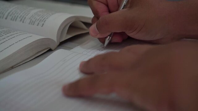 Hand holding a pen while writing notes on ruled paper indoors. Study footage capturing learning, journaling, and academic work in progress.