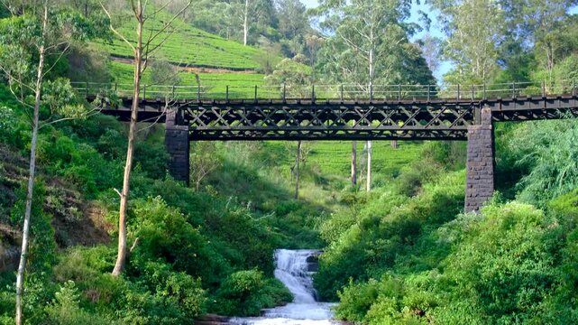 Scenic pan up Nanu Oya waterfall with cascading water to railway bridge in Nanuoya, highlands, Sri Lanka