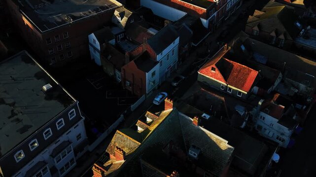 Oblique aerial view over historic rooftops and narrow streets in Salisbury city centre, with warm low-angle sunlight highlighting traditional buildings and tiled roofs