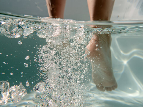 Underwater view of human legs and feet with bubbles in clear swimming pool water