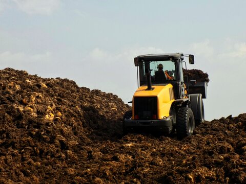 Yellow wheel loader moving organic compost heap at an industrial site
