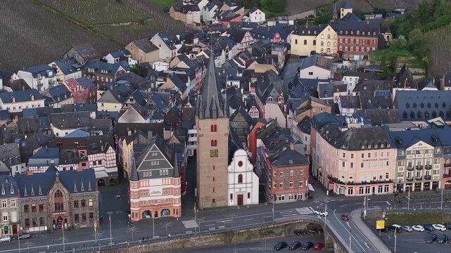 Aerial view of Bernkastel-Kues, Germany, showing the historic waterfront, St. Michael&rsquo;s Tower, Moselle River, stone bridge and vineyard-covered hills behind the old town.
