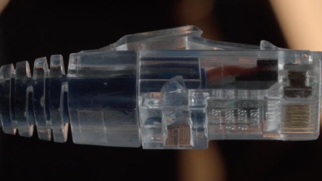 Close up of transparent Ethernet network cable connector showing RJ45 plug with visible metal contacts and internal wires against softly blurred background