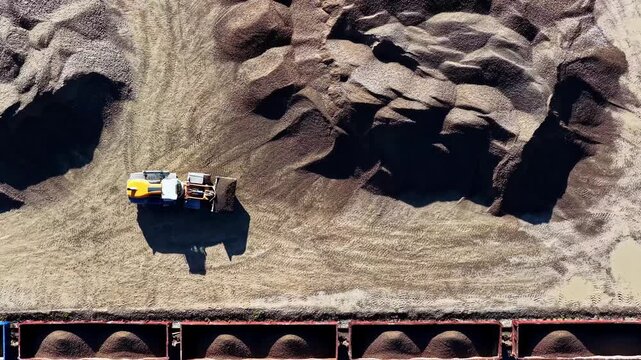 Aerial view of a yellow bulldozer working in a gravel quarry with piles of crushed stone and industrial machinery in Petrasiunai, Siauliu apskritis, Lithuania.