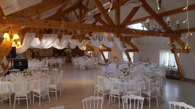 Round tables and string lights fill a decorated wedding hall near Paris, France, camera panning.