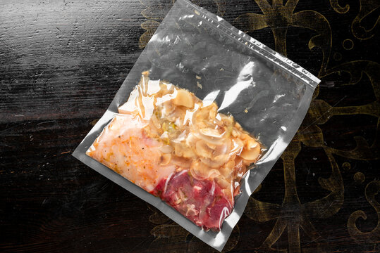 Vacuum sealed bag with marinated meat and sliced onions on a dark wooden background