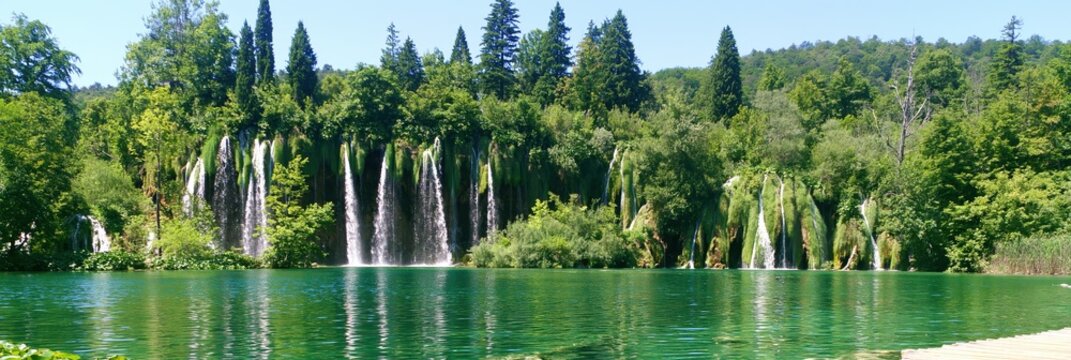 Cascading waterfalls flow into a vibrant green lake surrounded by