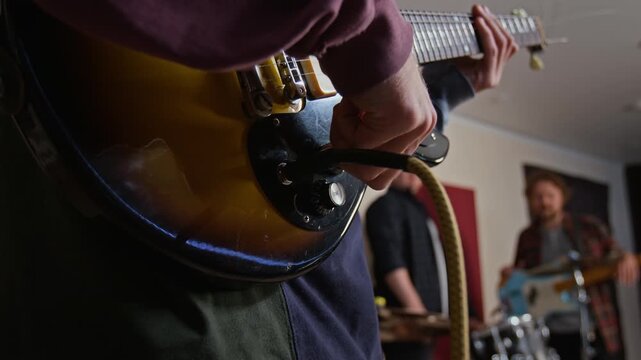Close-up view of unknown musician plugging audio jack cable into electric guitar during rehearsal. Footage serves music school promos, audio equipment commercials, and band marketing campaigns