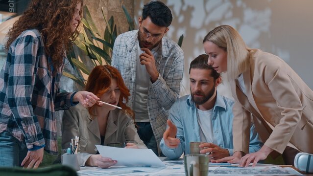 Stressed busy multiracial five coworkers in startup office casual informal business process women men talking discussing papers documents chaos group colleagues coworking working paperwork development