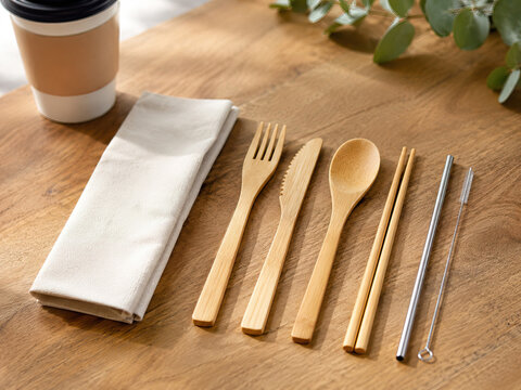 A set of reusable cutlery and drinking straws rests on a light brown wooden table, forming a travel kit. zero footprint, eco-friendly