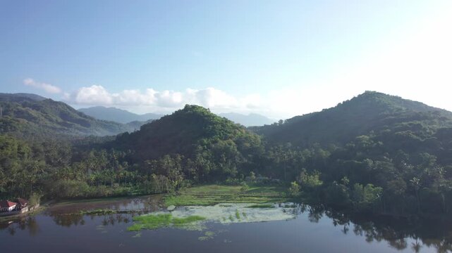 Aerial view of Danau Yeh Malet surrounded by lush green hills and calm water in Kecamatan Manggis, Bali, Indonesia.
