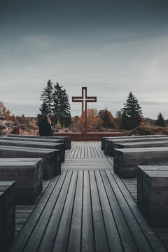 View of Vastseliina Episcopal Castle featuring a large wooden cross and rows of wooden benches with a person sitting quietly in Vana-Vastseliina, Voru County, Estonia.