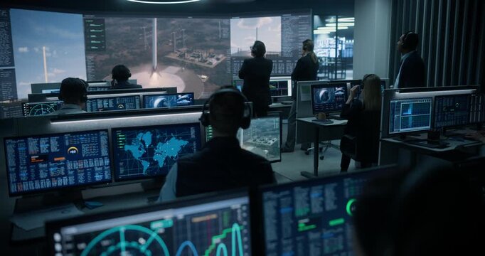 Monitoring Control Room. Female Specialist Analyzes Radar and Frequency Data on Dual Displays as Mission Control Staff Applaud a Reusable Rocket Booster Touching Down on the Big Screen.