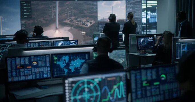 Monitoring Control Room: Diverse Flight Engineers in Headsets Track Telemetry, Radar and World Maps on Screens as a Reusable Rocket Booster Touches Down on the Landing Pad, Team Applauds.
