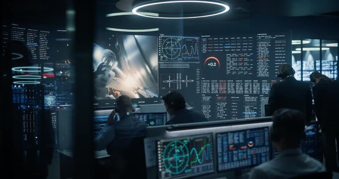 Monitoring Control Room: Aerospace Engineers Observe an Astronaut Conducting an Orbital Repair on Large Video Walls, Reviewing Radar Plots, Trajectory Graphs and Life Support Telemetry Readouts.